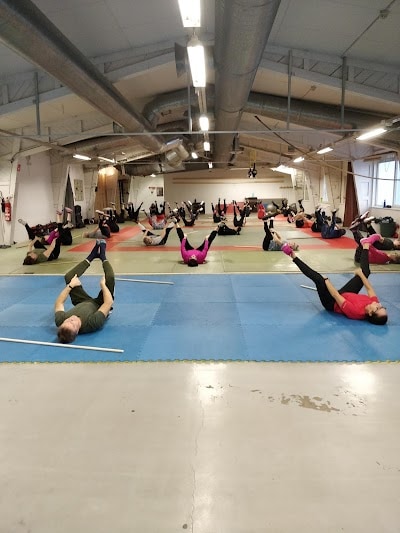 Ryhmäliikuntatunti salin keskellä, ihmiset venyttelemässä lattialla ja valmistautumassa harjoituksiin.