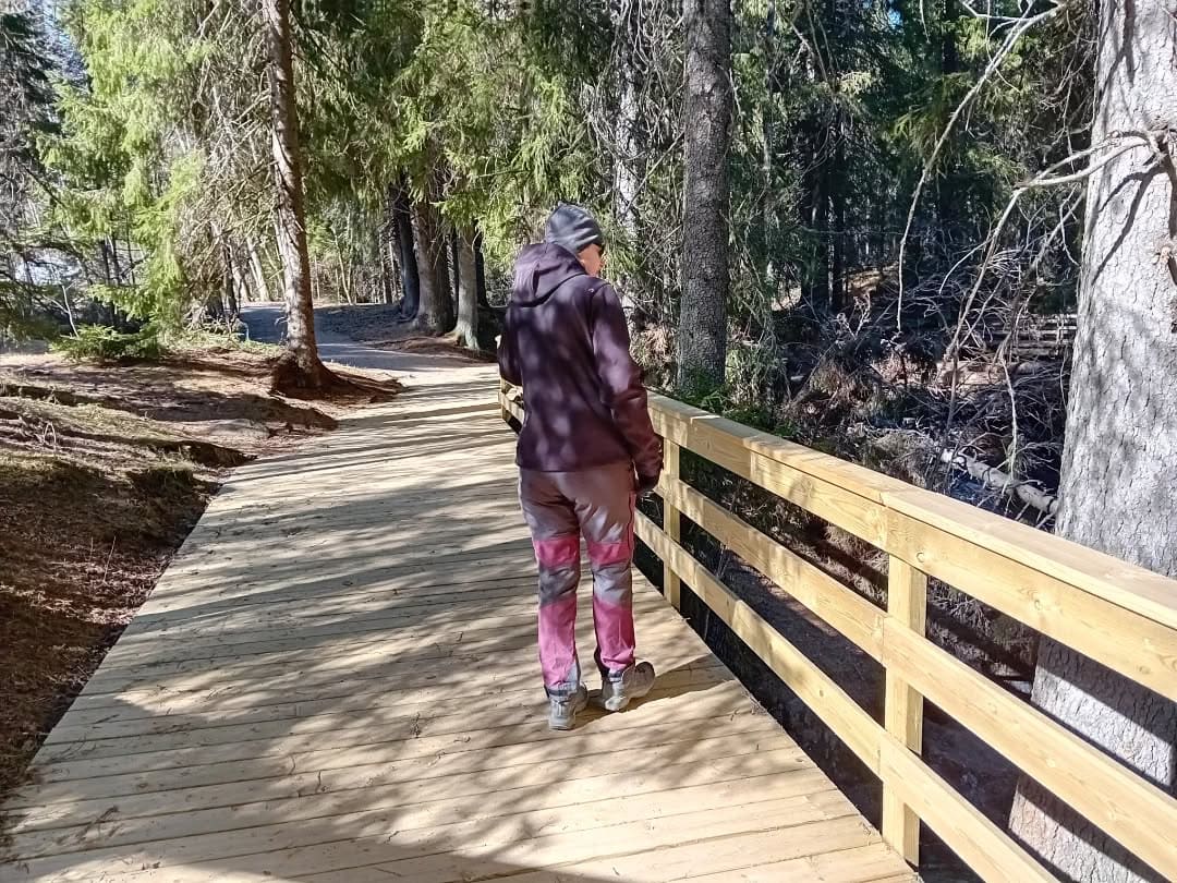 Kävijä kävelee luonnonkauniilla metsäpolulla puistossa, nauttien ulkoilmasta ja luonnon rauhasta.