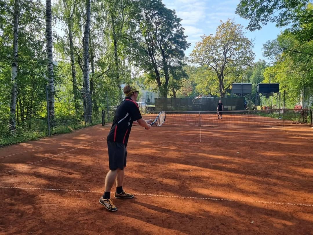 Ulkoilmatenniskenttä, jossa kaksi pelaajaa pelaamassa tennisottelua.