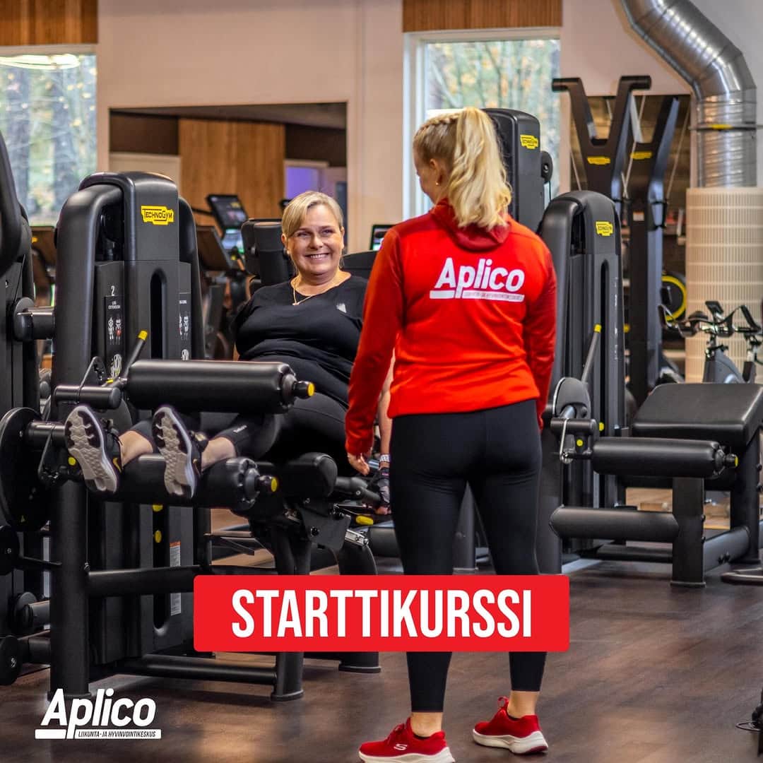 Nainen harjoittelee kuntosalilaitteella, ohjaaja avustaa.