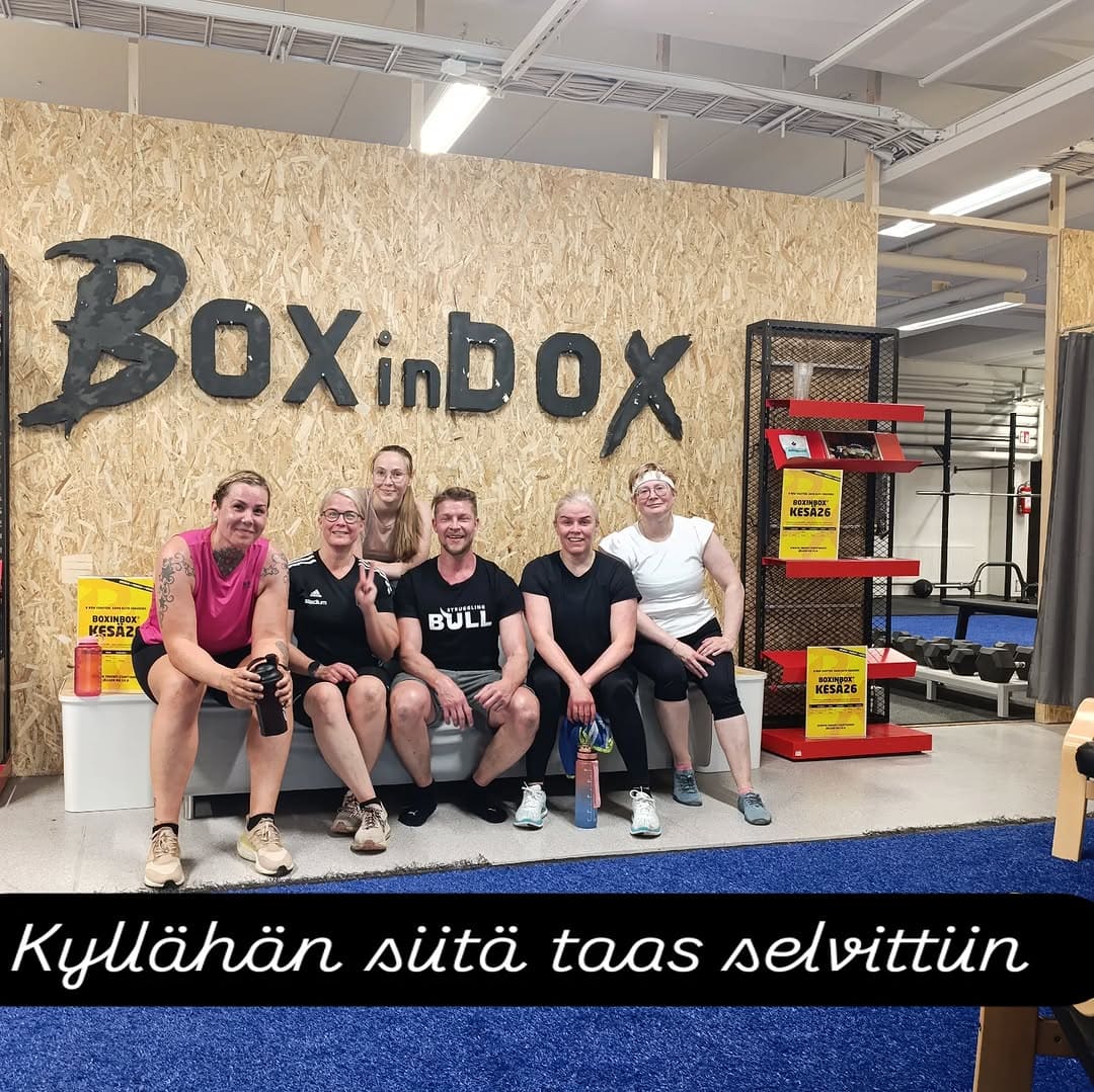 Ryhmä ihmisiä istuu kuntosalilla Box in Box -alueella, ystävällinen ilmapiiri.
