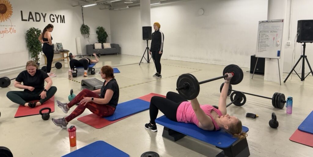 Nainen tekee painonnostoharjoituksia kuntosalilla ryhmässä.